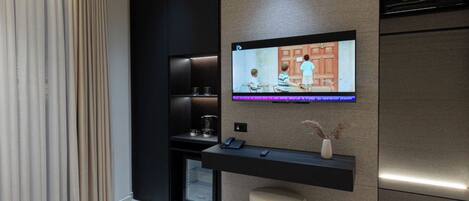 Una habitación de hotel moderna con una televisión de pantalla plana montada en la pared, una mesita de café, una mesita de noche y un ventanal grande con cortinas.