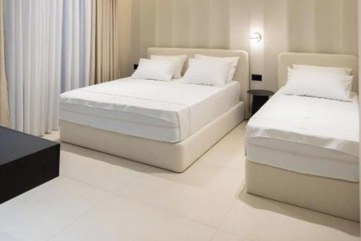 Un dormitorio moderno con dos camas, una mesita de noche y un ventanal con cortinas.