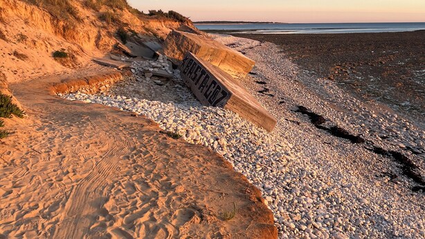 A beach with a wooden sign, pebbles, and sand.