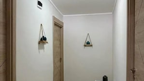 A hallway with a white bench, two doors, and wall-mounted shelves with items. - Rastgele Otel (Seferihisar)