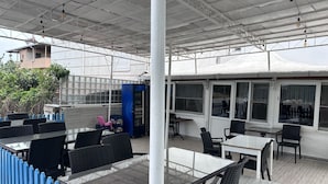 An outdoor dining area with tables and chairs, a blue fence, and a vending machine. - Rastgele Otel (Seferihisar)
