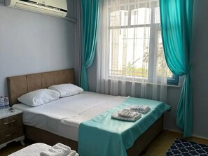 A neatly made bed with a teal bedspread, white pillows, and a folded towel on the side. - Rastgele Otel (Seferihisar)