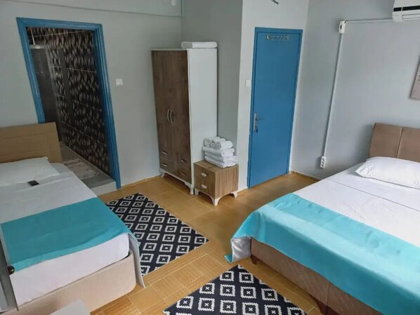 Una habitación con dos camas, un armario, una mesita pequeña con toallas y una alfombra estampada.