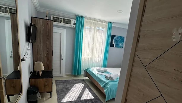 A bedroom with a bed, a dresser, a mirror, a TV, and a wardrobe. - Rastgele Otel (Seferihisar)