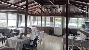 A restaurant with high ceilings, wooden beams, and large windows. Tables are set with white tablecloths and chairs. - Rastgele Otel (Seferihisar)