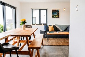 Un espacio habitable moderno con una mesa de comedor de madera, sillas negras, un sofá gris y una alfombra tejida.