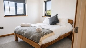 A bedroom with a wooden bed, two windows, and a view of the outdoors. - Modern balcony property, Sea views over Newgale (Newgale)