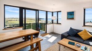 A modern living room with a large window, a sofa, a coffee table, and a dining table. - Modern balcony property, Sea views over Newgale (Newgale)