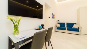 Een moderne woonkamer met een flatscreen televisie aan de muur, een eettafel met stoelen, een blauwe bank en een bloevas.