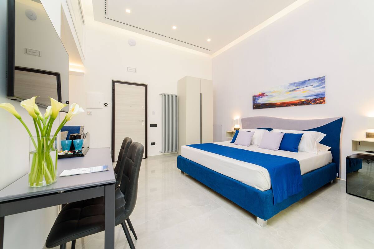 A modern hotel room with a large bed, a desk, and a chair.
