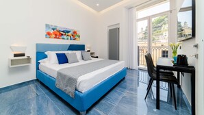 Een moderne slaapkamer met een groot bed, een schilderij erboven, een bureau met stoel en een balkon met uitzicht op gebouwen.
