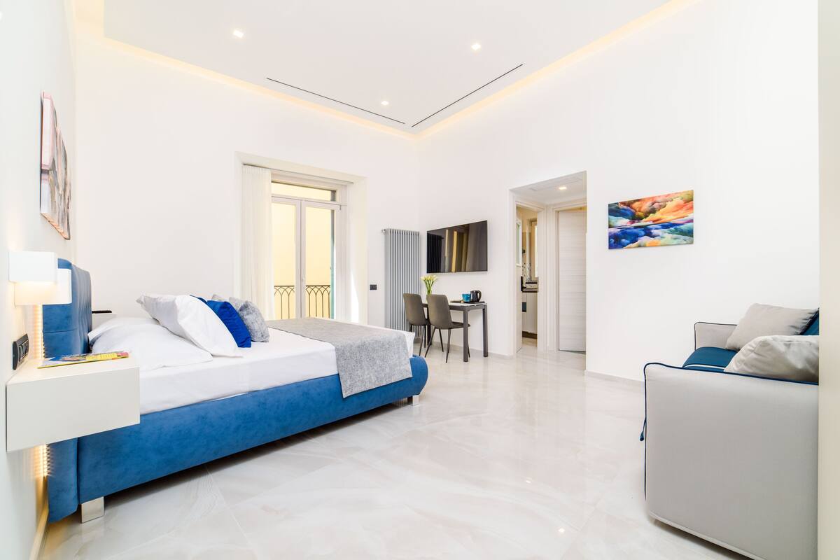 A modern hotel room with a large bed, a desk, and a seating area.
