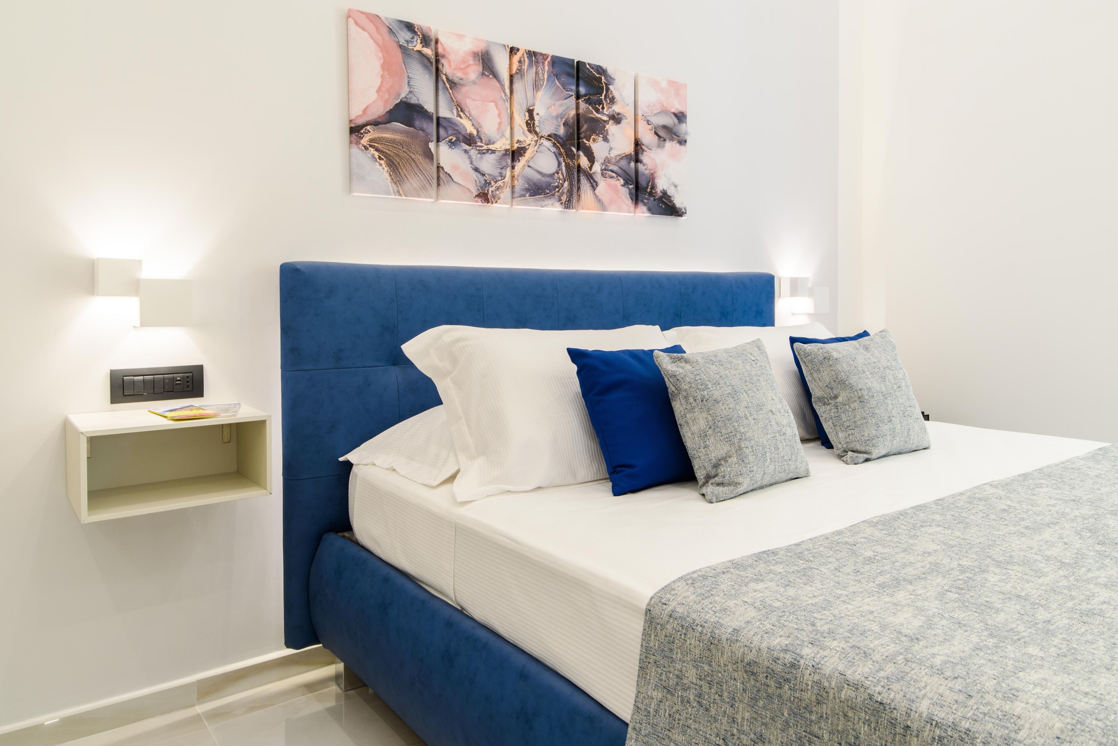 Ein Schlafzimmer mit blauem Kopfteil, weißer Bettwäsche und einer grauen Tagesdecke.