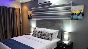 Ein modernes Hotelzimmer mit einem großen Bett, einem Nachttisch mit Lampe, einer Klimaanlage und einem Bild an der Wand.