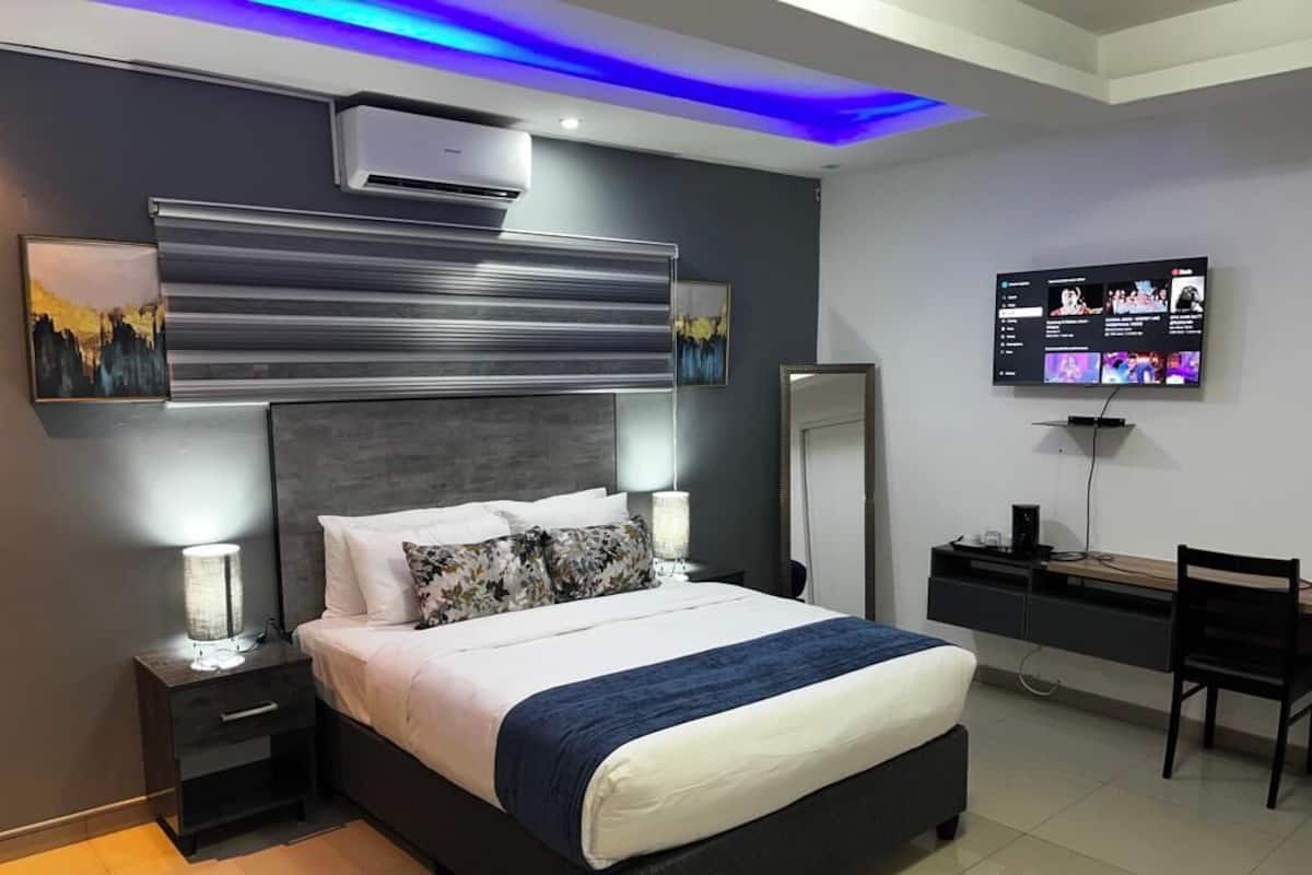 Un dormitorio moderno con una cama grande, mesitas de noche con lámparas, un televisor de pantalla plana y un escritorio con silla.