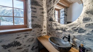 Een rustieke badkamer met een stenen muur, een houten raam en een stenen wastafel.