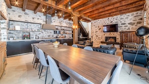 Een rustiek interieur met zichtbare houten balken, een stenen muur, een keuken met moderne apparatuur en een gezellige zithoek met leren banken.