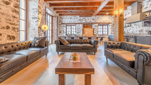 Een ruime woonkamer met een grote leren bank, een houten salontafel en een stenen muur.
