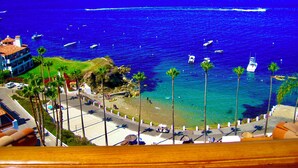 Vista costeira com praia, palmeiras e barcos na água.