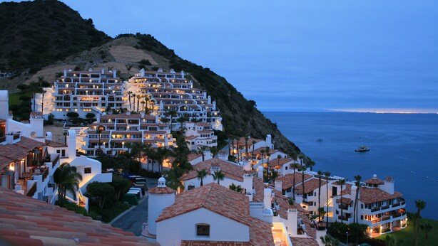 Uma cidade costeira com edifícios de vários andares, alguns com varandas, e vista para o mar.