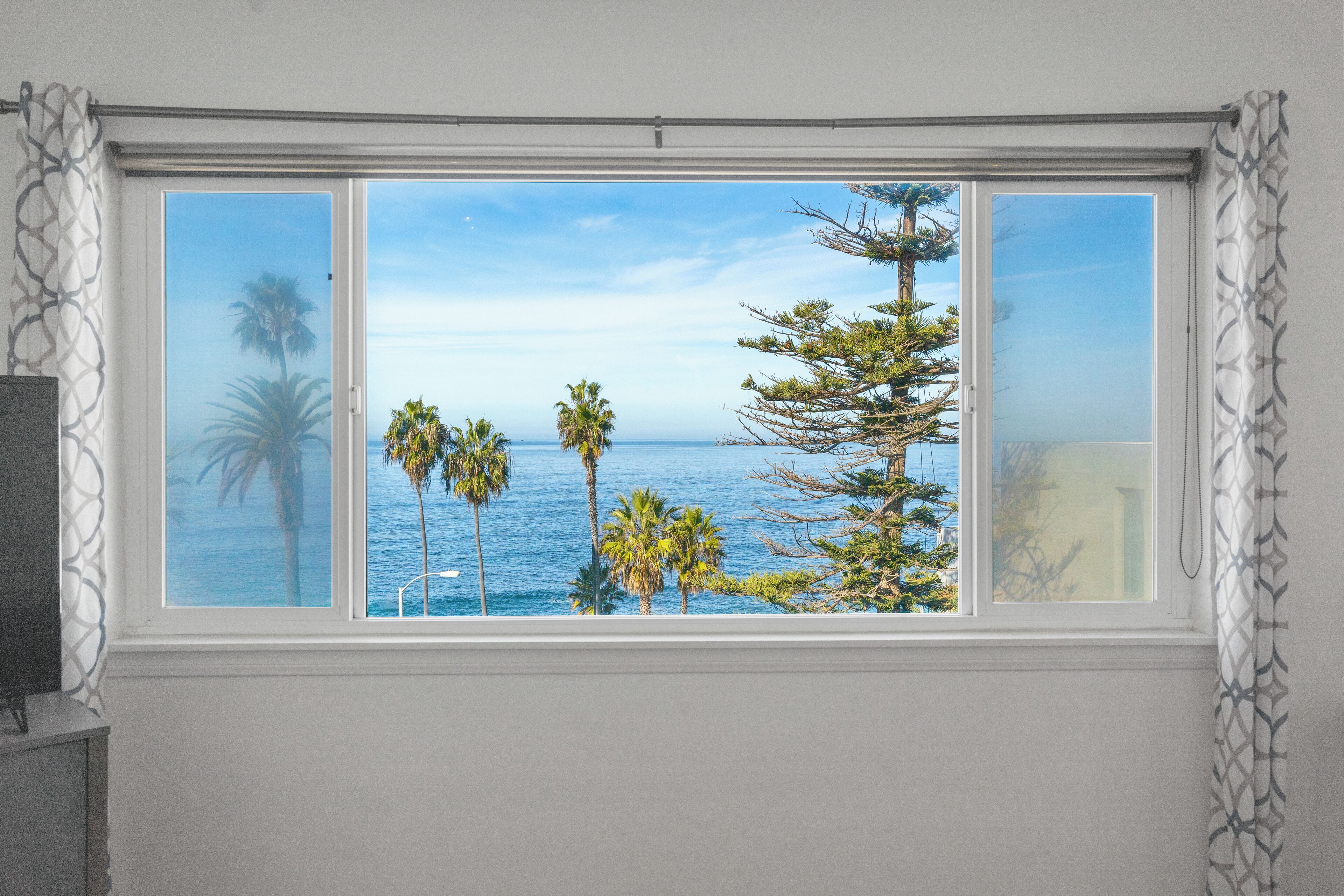 A room with a large window offering a view of the ocean and palm trees.