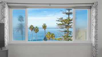 A room with a large window offering a view of the ocean and palm trees.