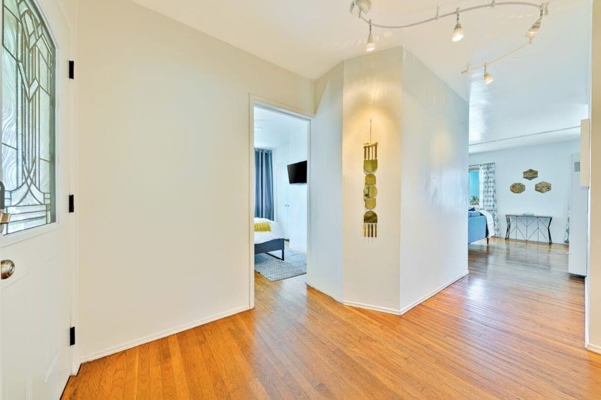 A spacious hallway with wooden flooring, a door with a glass window, and a wall-mounted light fixture.