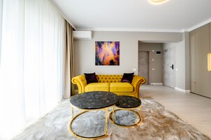 Una sala de estar moderna con un sofá amarillo, dos mesas de mármol negro y un cuadro abstracto de colores en la pared.