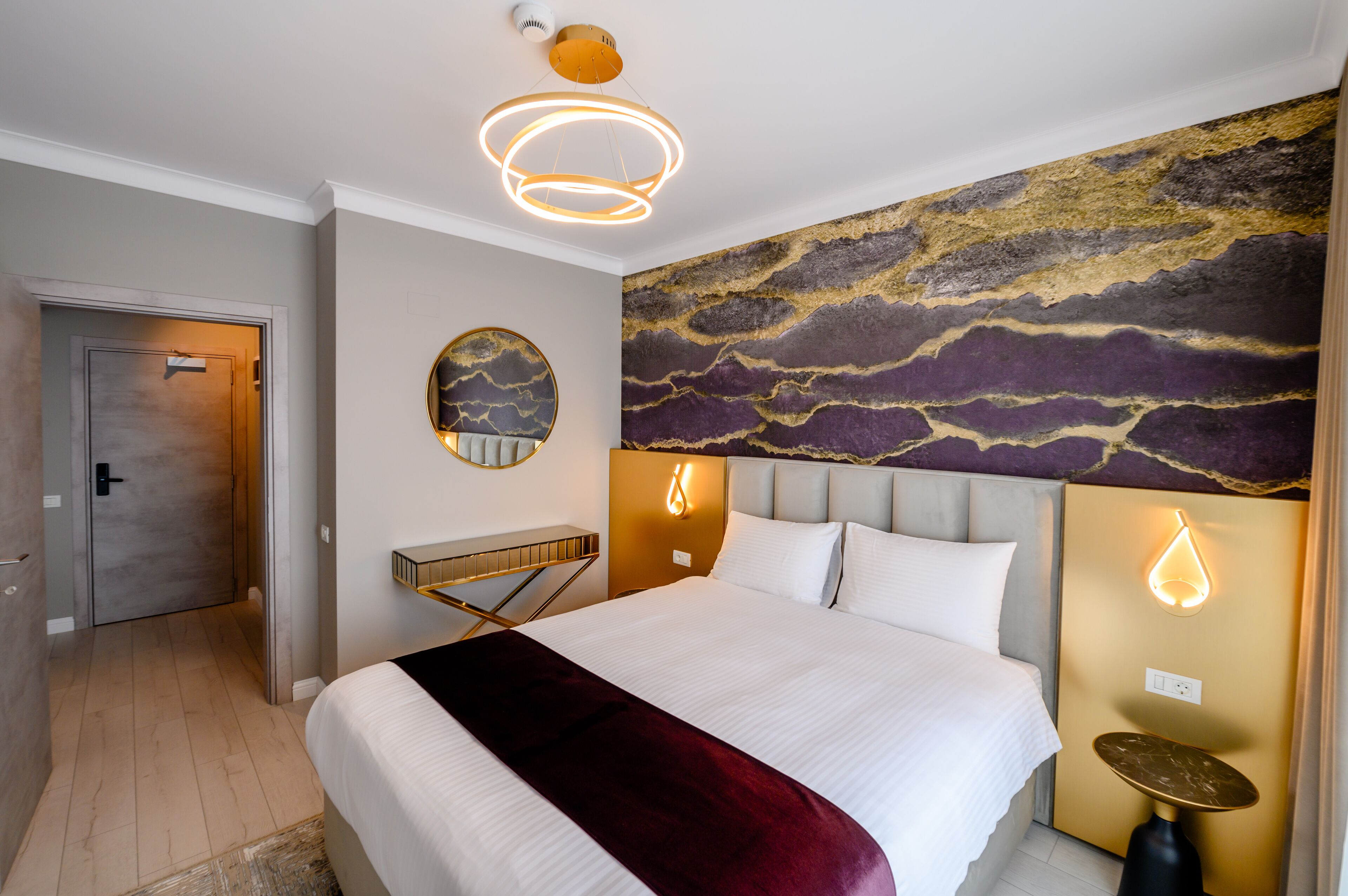 Et moderne hotelværelse med en stor seng, et rundt spejl, et unikt vægmaleri og en loftlampe.
