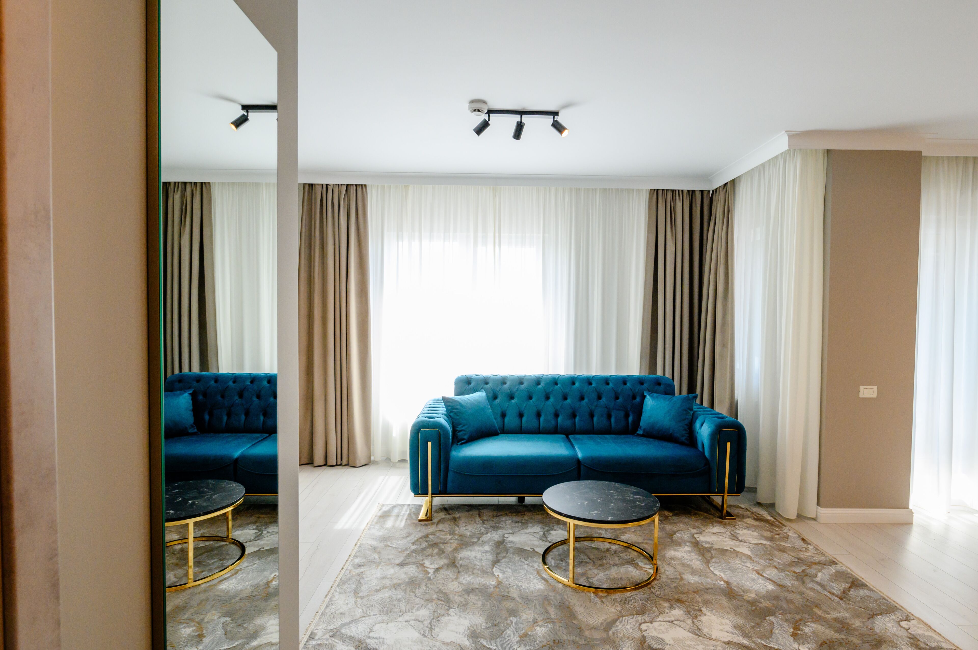 Uma sala de estar moderna com um sofá azul, duas mesas redondas e um lustre.