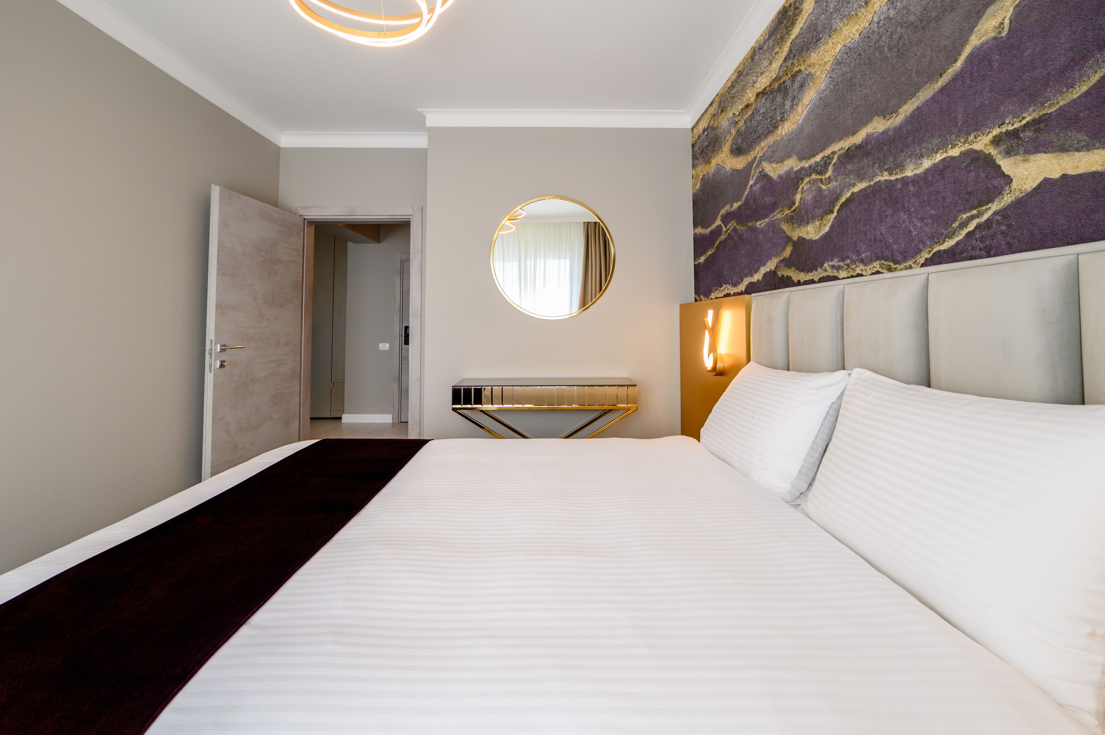 A hotel room with a large bed, a round mirror, a wall-mounted light, and a marble-patterned wall.