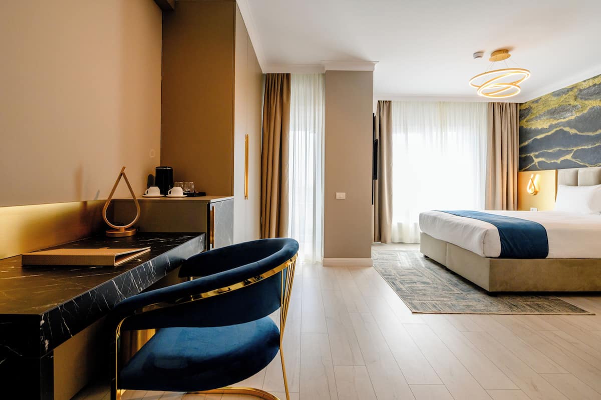 A hotel room with a bed, a desk with a chair, a coffee maker, and a painting on the wall.
