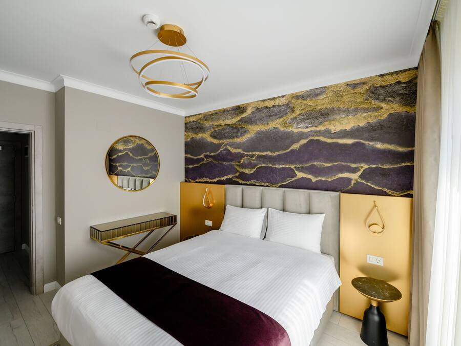 Una habitación de hotel moderna con una cama grande, un espejo redondo, un mural único en la pared y una lámpara de techo elegante.
