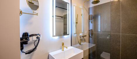 Een moderne badkamer met een witte wastafel, gouden details, een haardroger en een douche met glazen wanden.
