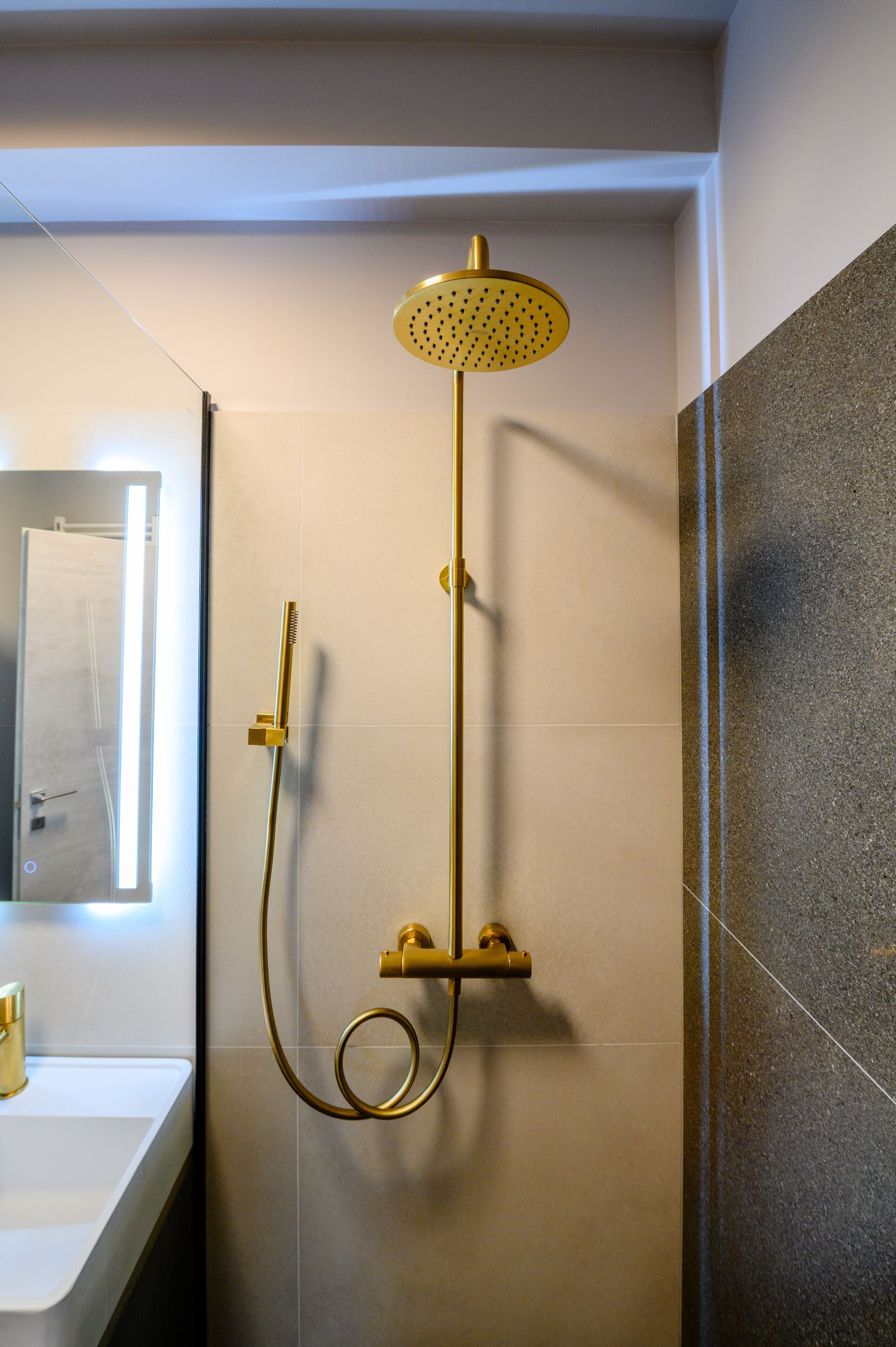 Een moderne badkamer met een gouden douchekop, een handdouche en een spiegel aan de wand.
