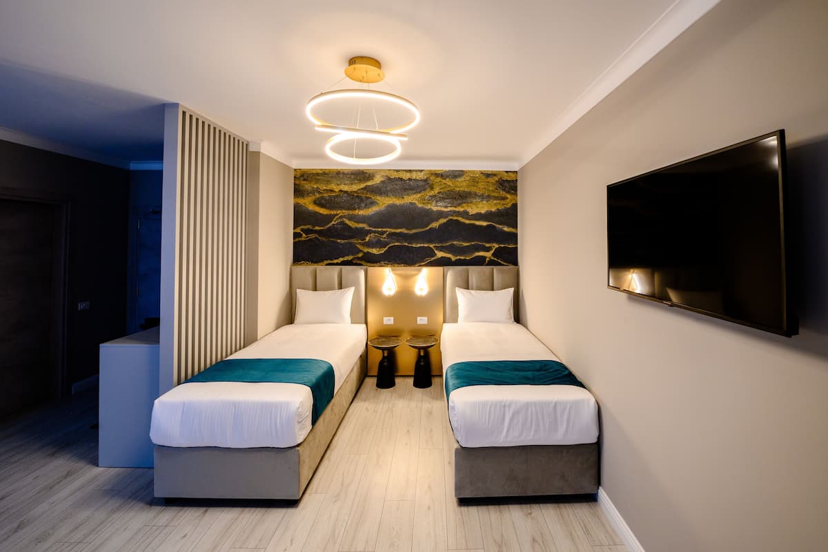 A modern hotel room with two beds, a large wall-mounted TV, and a unique ceiling light fixture.