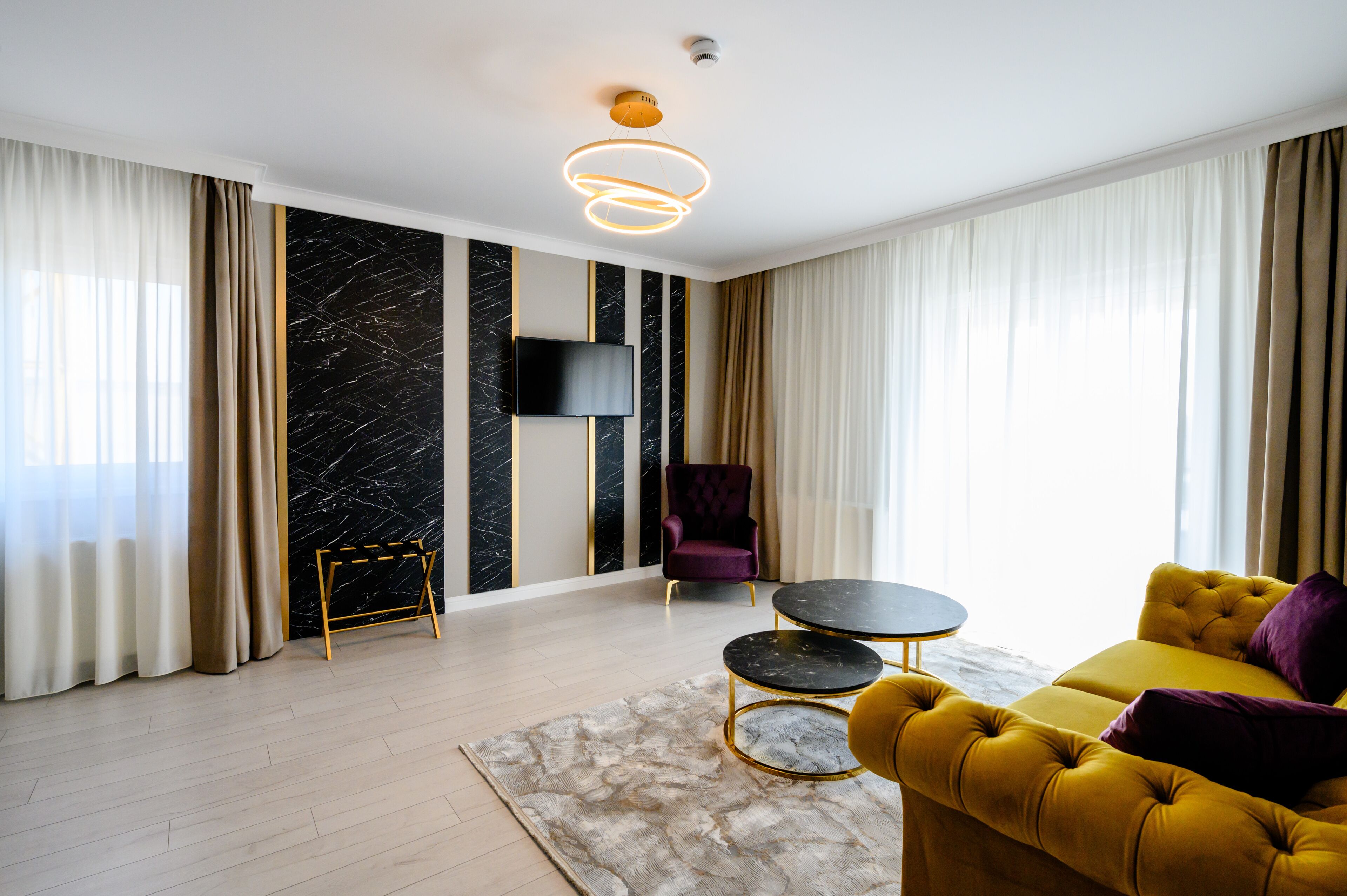 A modern living room with a yellow sofa, a round coffee table, a purple armchair, and a flat-screen TV mounted on the wall.