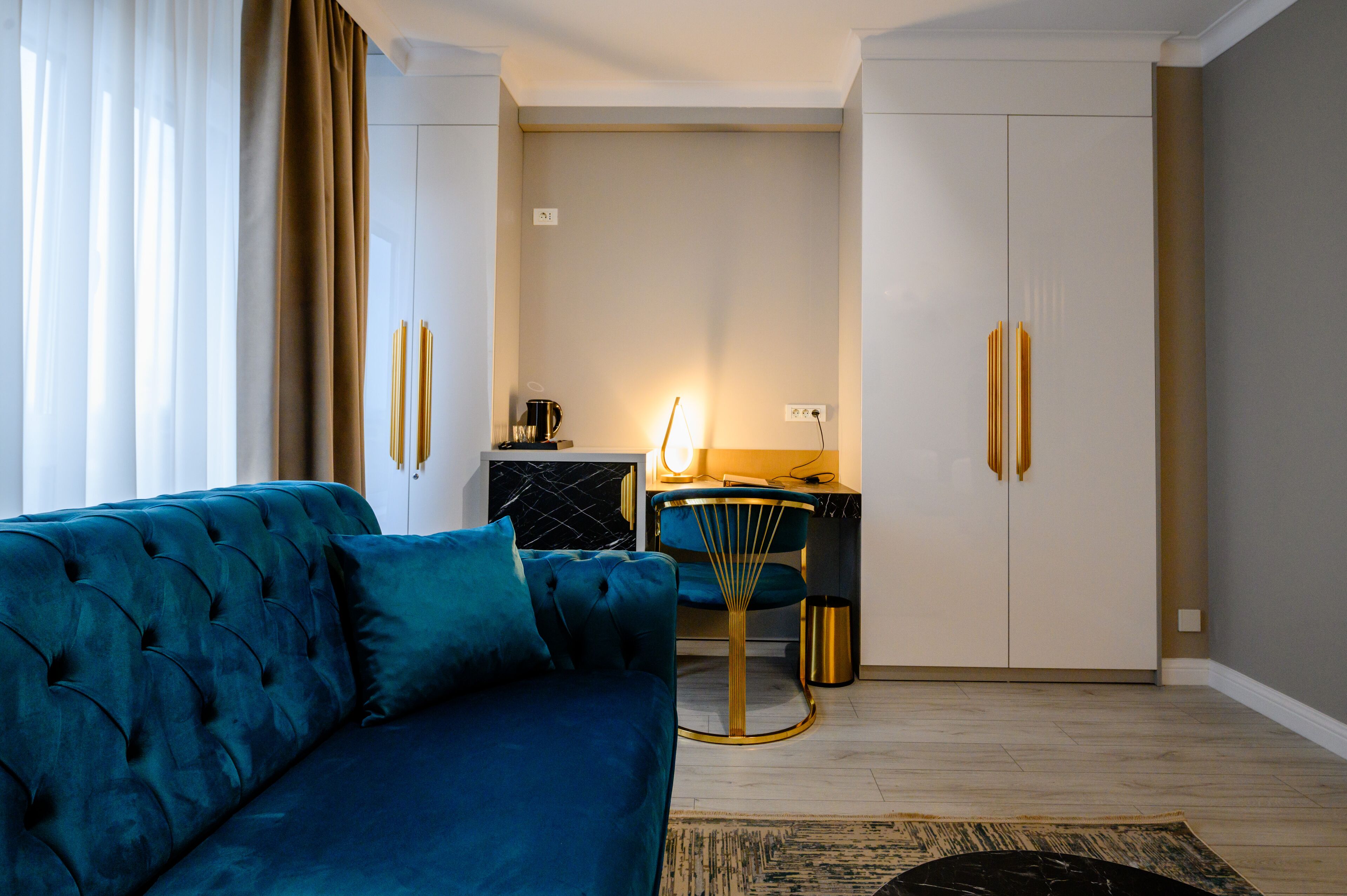 A modern living room with a blue sofa, a small round table with a lamp, and a kitchen area in the background.