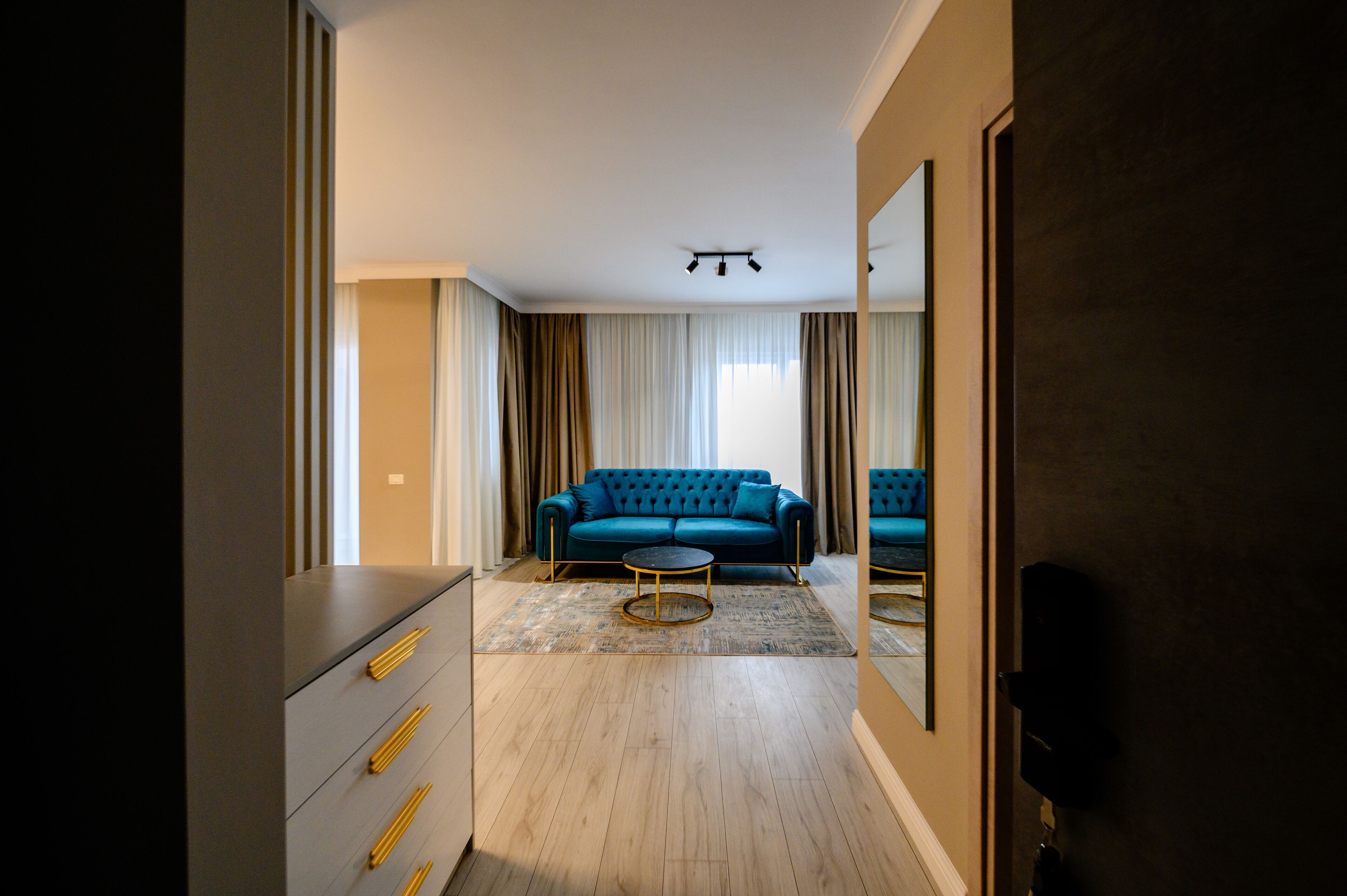 Una camera d'albergo moderna con un divano blu, un tavolino rotondo e uno specchio grande.