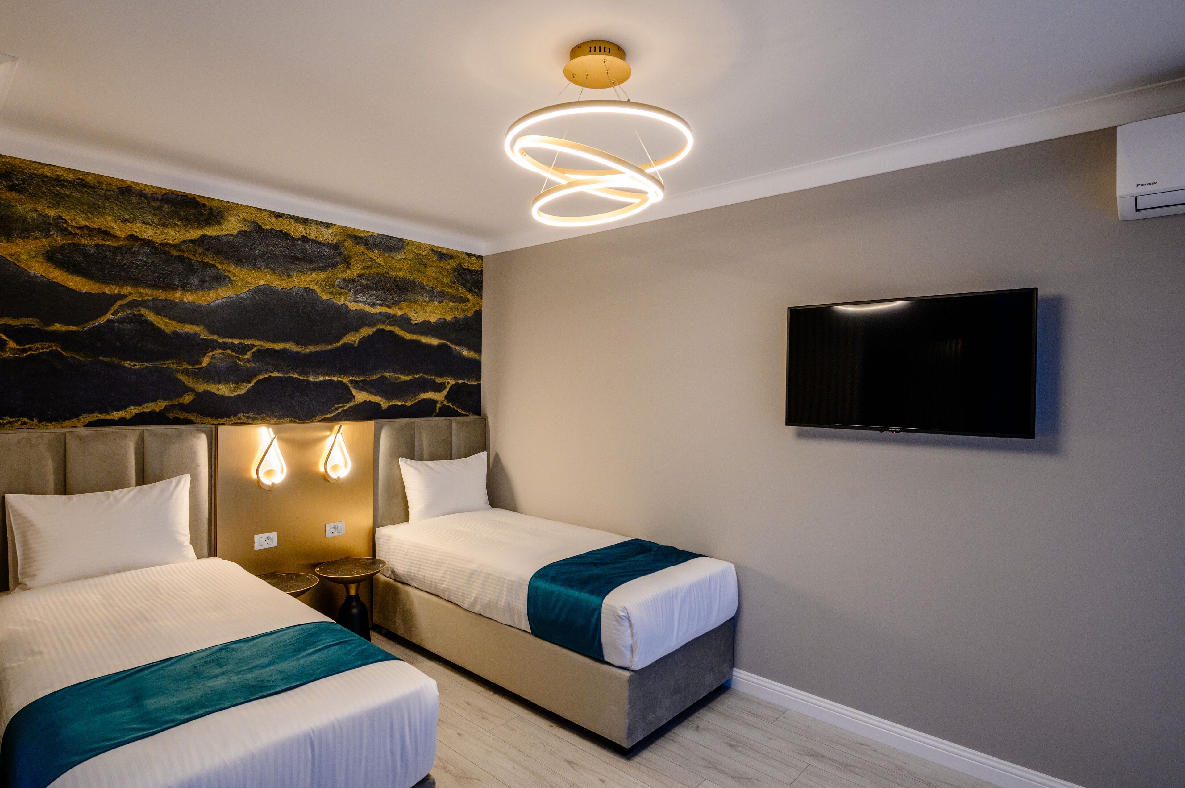 A hotel room with two beds, a modern light fixture, a flat-screen TV, and a decorative wall mural.