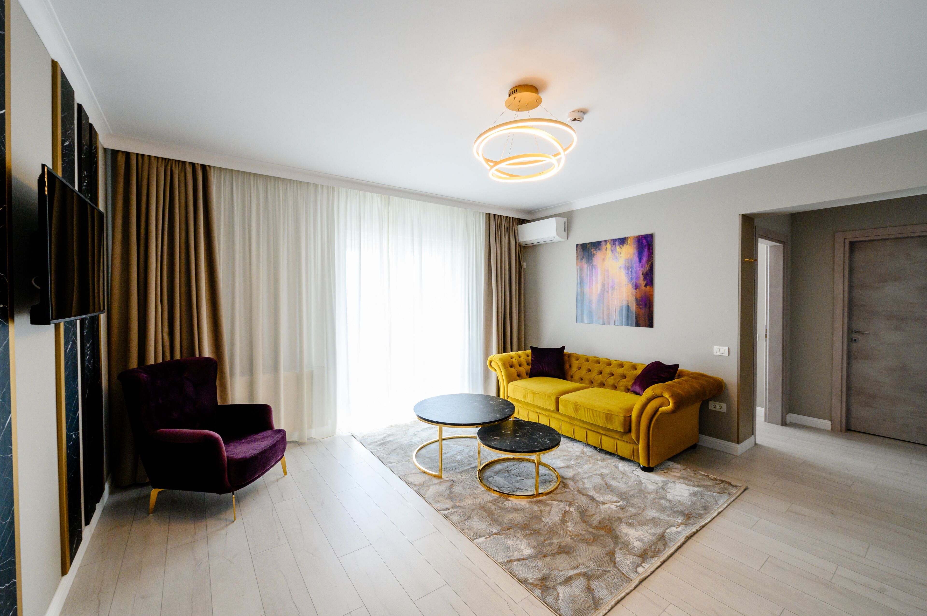 A modern living room with a yellow sofa, a purple armchair, and two black round tables.