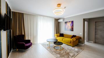 A modern living room with a yellow sofa, a purple armchair, and two black round tables.