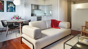 Uma sala moderna com sofá, mesa de jantar com cadeiras, cozinha e mesa de centro de vidro.