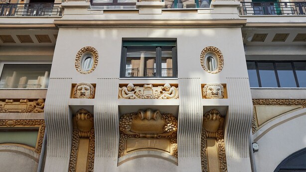 Fachada de edifício com esculturas elaboradas, uma janela central e duas varandas com grades.