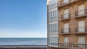 Um edifício à beira-mar com várias varandas, vista clara para o oceano e um calçadão à beira da água.