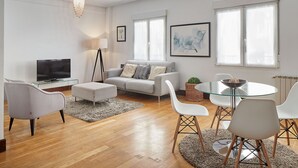 A modern living room with a sofa, TV, and glass dining table.