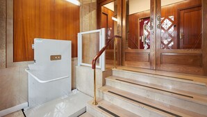 A hotel entrance with a wooden door, a glass door with a geometric pattern, and a set of marble stairs with a handrail.