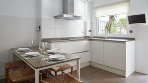 A modern kitchen with white cabinetry, a stainless steel range hood, a window with a view, and a dining area with a table set for four.