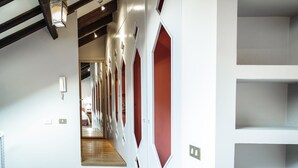 A hallway with white walls, red accents, and wooden beams. There are multiple doors with geometric patterns and a hanging lantern. - San Fermo Apartment (Milan)