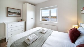 A bedroom with a bed, a dresser, a window with a view, and a painting on the wall. - Fresh & Stylish | Ocean View | Donegal Town & Bay (Tullycullion)